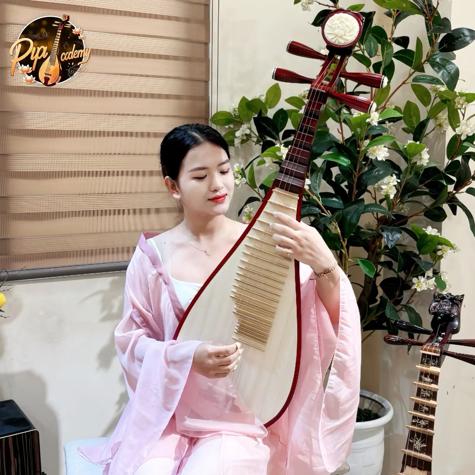 Người chơi đàn mặc áo lụa hồng mỉm cười, đặt tay trên phím cây đàn tỳ bà viền đỏ