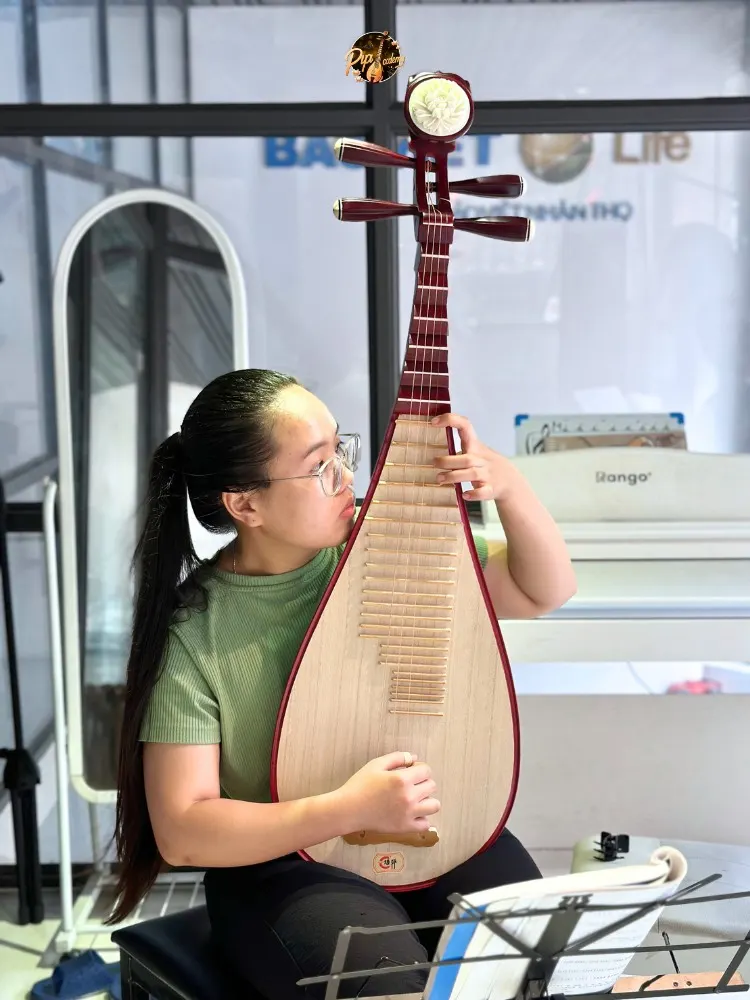 Người chơi đàn buộc tóc đuôi ngựa, mặc áo xanh lá, tập đàn tỳ bà trước giá nhạc