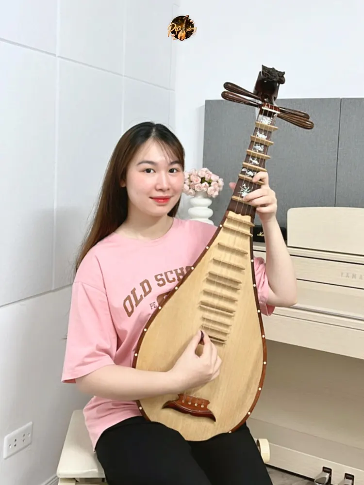 Người chơi đàn mặc áo phông hồng ôm cây đàn tỳ bà trong phòng học có đàn piano