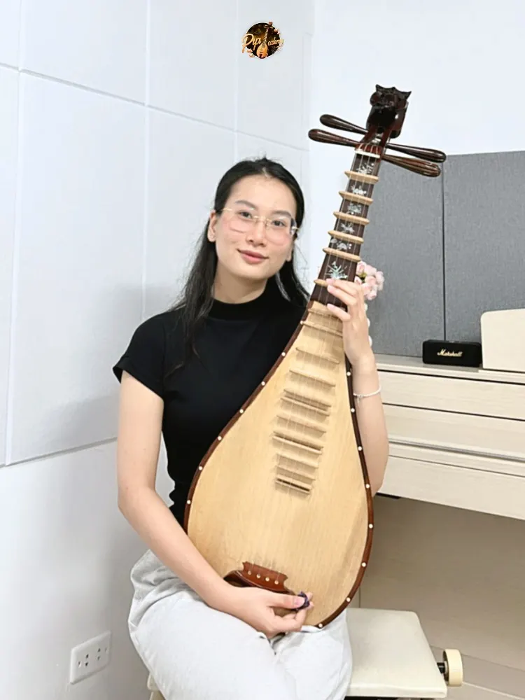 Người chơi đàn mặc áo đen, đeo kính, mỉm cười ôm cây đàn tỳ bà trong phòng học