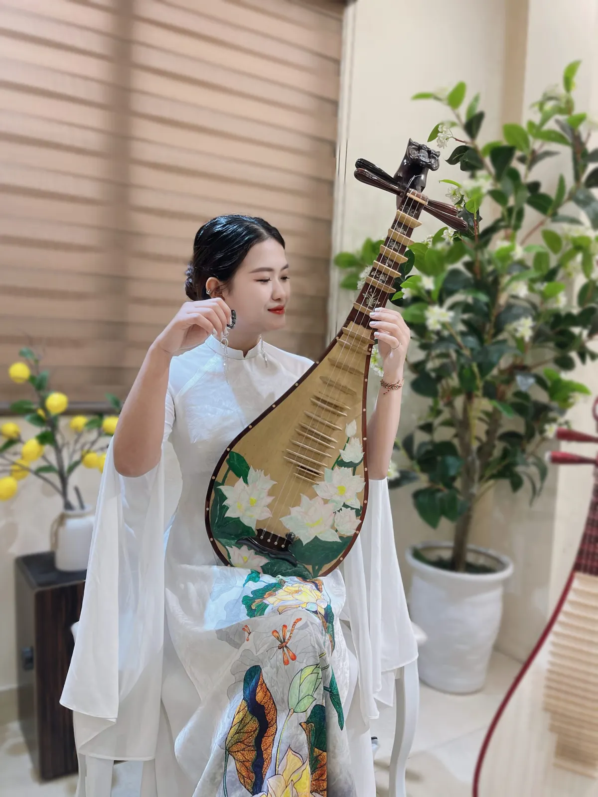 Người chơi đàn mặc áo dài trắng hoạ tiết sen, lên dây cây đàn tỳ bà vẽ hoa sen
