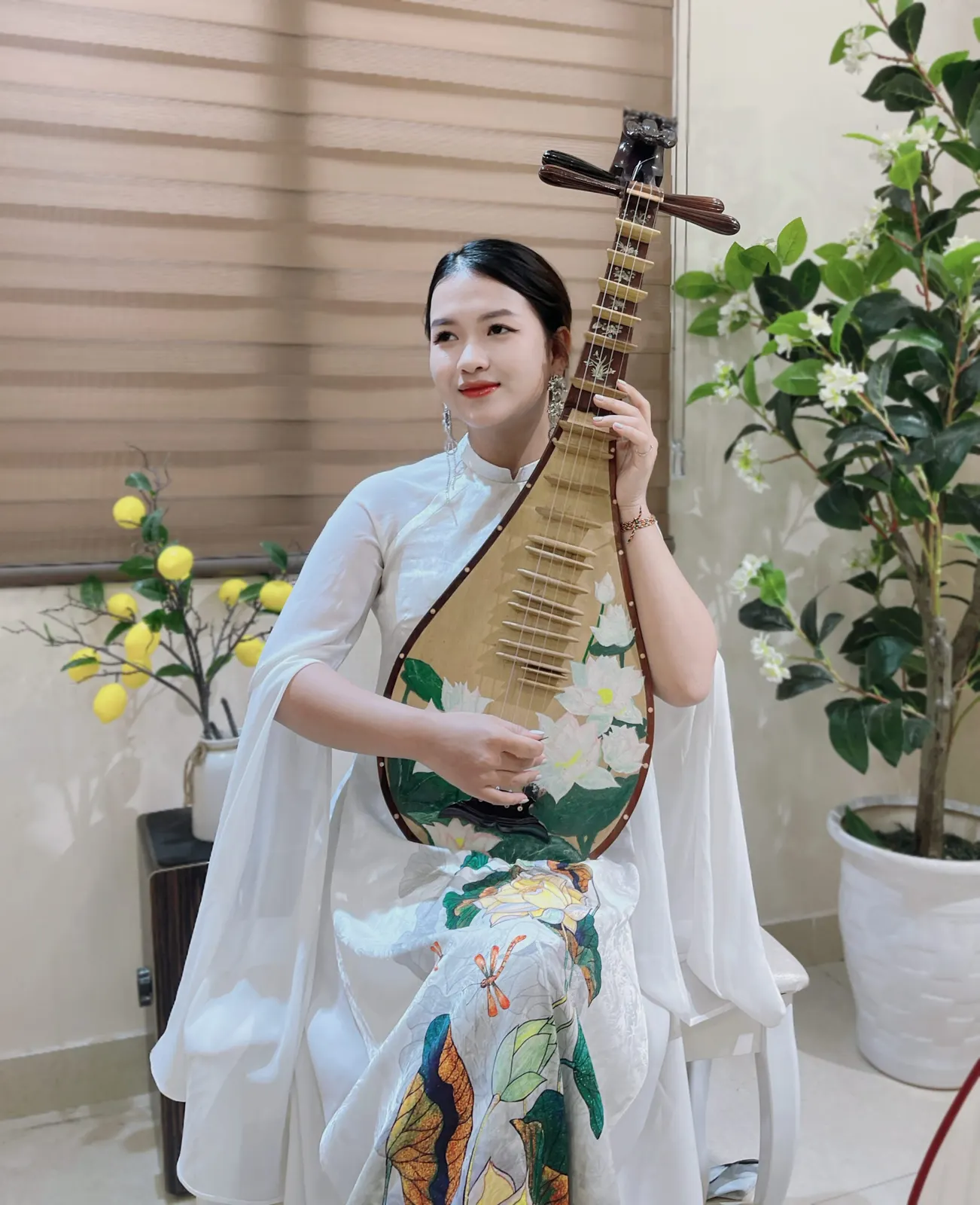 Người chơi đàn mặc áo dài trắng mỉm cười, ôm cây đàn tỳ bà vẽ hoa sen