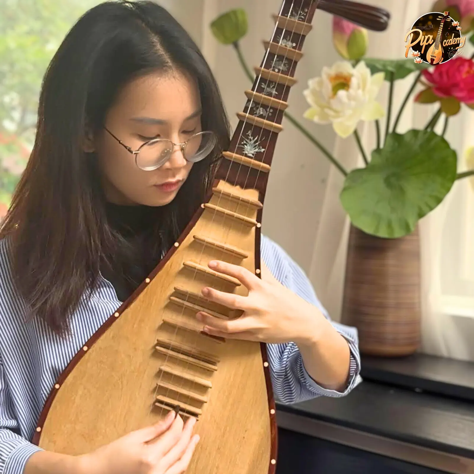 Đôi tay bấm phím và gảy dây trên cây đàn tỳ bà khảm hoa, phía sau là bình hoa sen