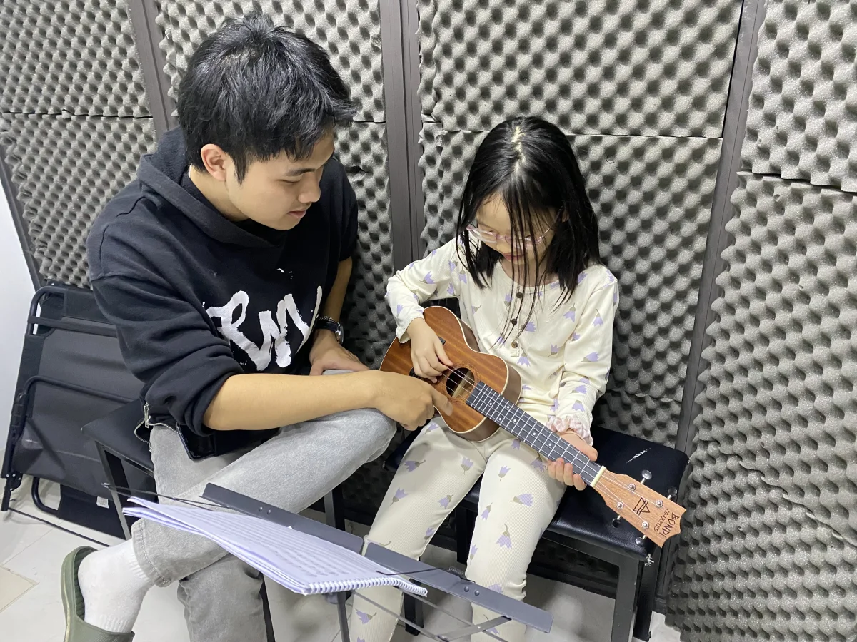 Giáo viên hướng dẫn học viên cách chơi dây đàn ukulele