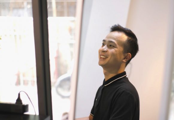 Người mặc áo polo đen tươi cười trong phòng học cạnh cửa sổ