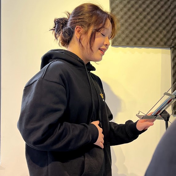 Bạn nữ áo hoodie đen đặt tay lên bụng, luyện hơi thở khi hát trong phòng cách âm