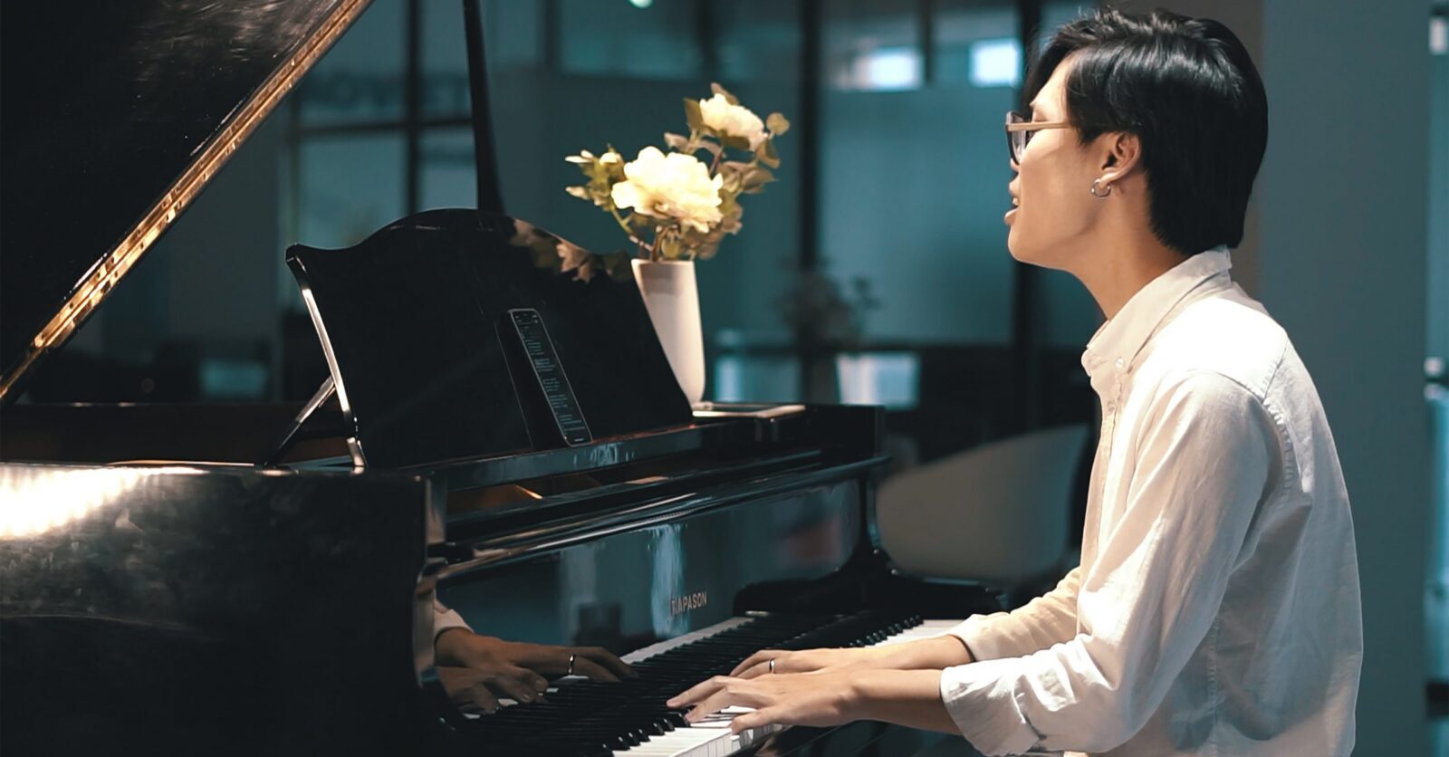 Người đeo kính, áo sơ mi trắng vừa đệm grand piano vừa hát